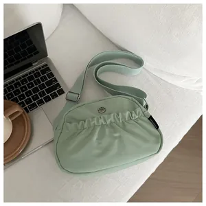 Detail of light green pleated crossbody bag with metal logo and wide adjustable strap