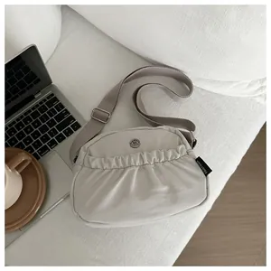 Detail of a beige ruched crossbody bag with adjustable wide strap and metal logo