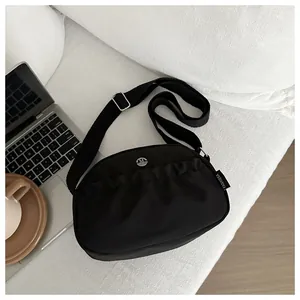 Detail of black pleated crossbody bag with adjustable strap and metallic logo accent