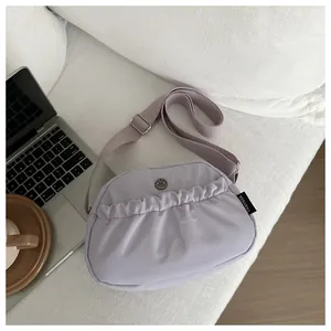 Detail of lilac pleated crossbody bag with metal logo on a soft white background