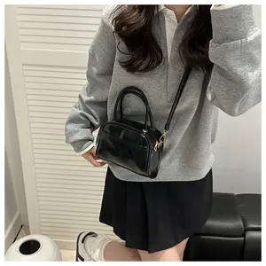 Polished black rectangular handbag with top handles and adjustable strap on a model