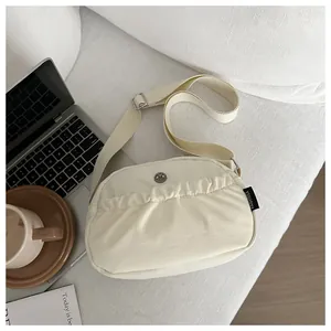 Detail of off-white ruched crossbody bag featuring metal badge and wide strap