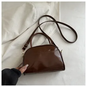 Detail of a brown glossy leather handbag with gold metal zippers and detachable strap