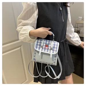 Detail view of blue plaid canvas mini backpack featuring red apple embroidery and strap