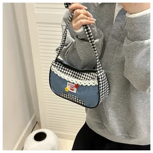 Close-up of denim shoulder bag with plaid pattern, lace trim, and cherry patch detail