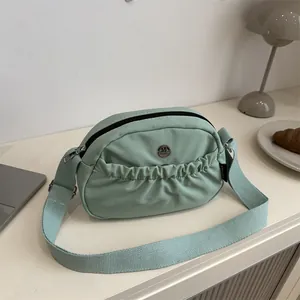 Minimalist pleated mint green crossbody bag with woven strap and metallic M detail
