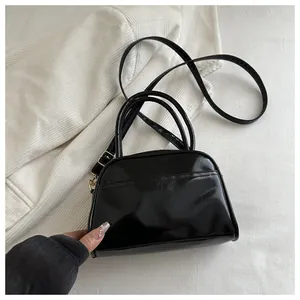 Detail of a minimalist black glossy crossbody handbag with elegant gold metal hardware