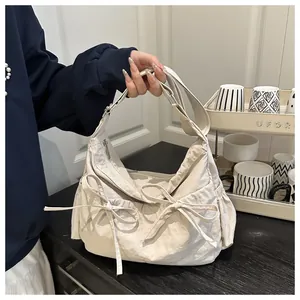 Close-up of cream nylon crescent bag featuring dual bow details and side drawstring pockets