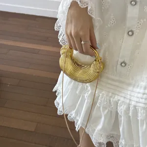 Detail of a golden half-moon evening bag with textured stripes and circular handle