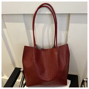 Detail of burgundy tote bag with faux crocodile texture on a black stylish chair