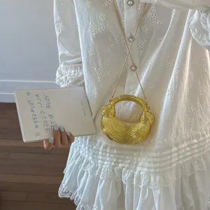 Golden crescent handbag with spiral texture and chain strap on a white lace dress