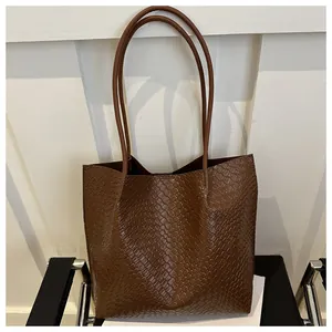 Close-up of brown leather tote bag showing woven texture and sleek shoulder straps
