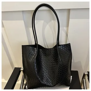 Detail of black woven leather tote bag showing fine texture and long shoulder straps