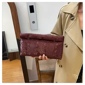 Detail of red-brown faux snakeskin envelope clutch bag held by model in trench coat