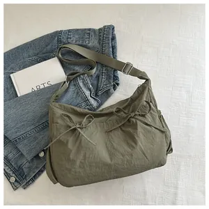 Close-up of olive green nylon crossbody bag with chic bow details on a fabric background