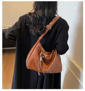 Detalle del bolso hobo marrón caramelo con textura de cuero y colgante de borla tejida