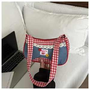 Detail of blue denim shoulder bag with red plaid trim, lace edge, and cherry patch