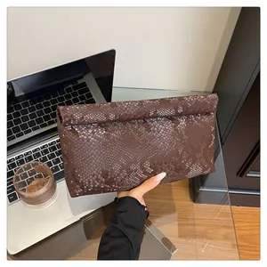 Close-up of deep brown snakeskin pattern envelope clutch bag in a stylish office setting