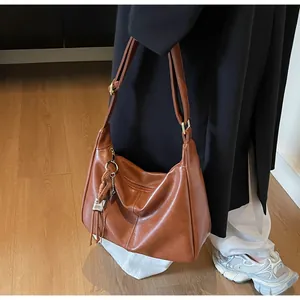 Detalle de bolso bandolera de cuero marrón con textura vintage y colgante de borla moderno