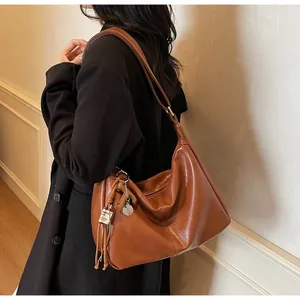 Bolso hobo marrón caramelo con detalle de flecos y logotipo metálico en una modelo