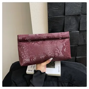 Detail of burgundy snakeskin envelope clutch with gold metal rings on a magazine
