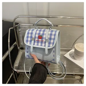 Detail of light blue mini backpack with red apple embroidery and blue plaid pattern lid