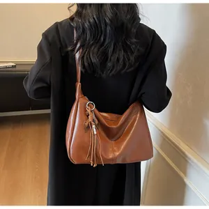 Detalle de bolso de hombro en cuero marrón con flecos decorativos y aro metálico