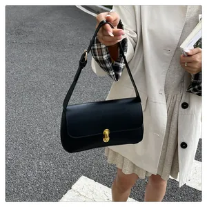 Detail of a black faux leather baguette bag featuring a gold twist-lock and shoulder strap