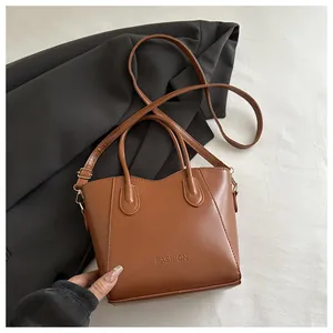 Detail of caramel brown bucket bag with FASHION embossing and gold metal buckles