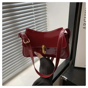 Detail view of deep red patent leather shoulder bag with a polished golden twist lock