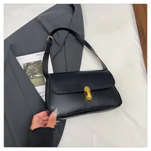 Top view of a minimalist black leather shoulder bag with a gold metal clasp on a grey blazer