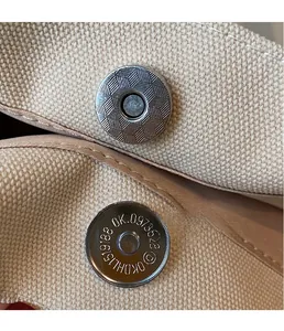 Vue macro du fermoir magnétique argenté et de la toile beige sur le sac cabas