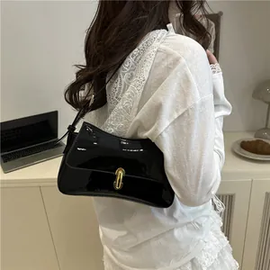Glossy black patent leather shoulder bag with gold clasp shown on a model
