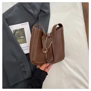 Close-up of brown leather bucket bag with white stitching and wavy gold metal buckle