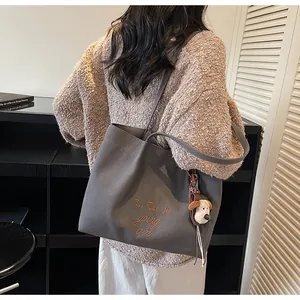 Détail d'un cabas en toile grise avec broderie marron et petit pendentif de chiot