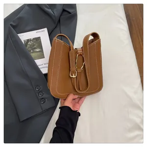 Detail of brown leather bucket bag featuring white contrast stitching and gold buckle