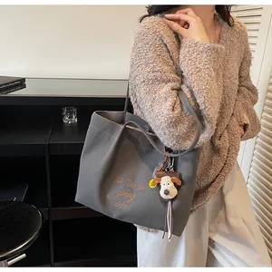 Gros plan d'un cabas en toile gris foncé avec broderie marron et breloque peluche