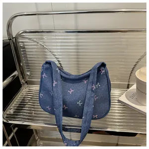 Detail of blue denim hobo bag featuring sweet pink and white bow patterns on metal shelf