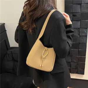 Beige semicircular shoulder bag with gold metal ring and tassels on black blazer model