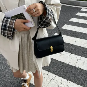 Minimalist black leather shoulder bag with gold clasp shown in a stylish street setting