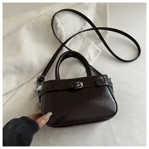 Détail d'un petit sac bandoulière marron brillant avec doubles anses et boucles argentées