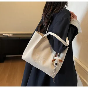 Détail du sac cabas en toile blanc cassé avec broderie cursive et breloque chien en peluche