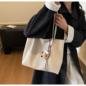 Détail d'un sac cabas en toile avec broderie et breloque chiot en peluche sur manteau noir