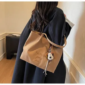 Détail d'un cabas en toile camel avec broderie cursive noire et charme de chien en peluche