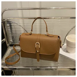 Brown litchi grain leather bag detail with gold buckle on a minimalist glass shelf