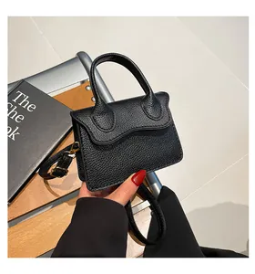 Détail d'un mini sac à main noir en cuir grainé avec rabat ondulé et finitions dorées