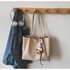 Détail de la broderie sur un sac cabas en toile beige suspendu à un support en bois