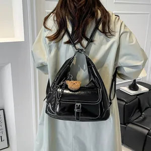 Versatile black glossy handbag with white stitching and brown bear charm on model