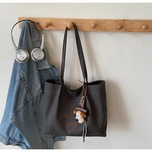 Détail d'un sac cabas en toile grise avec broderie marron et charm de chien mignon