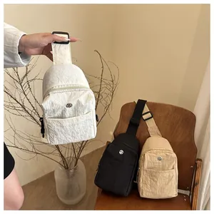 Three textured nylon crossbody bags in white, black, and beige on a wooden chair
